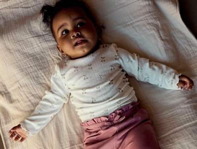 Baby iklædt Name It body i råhvid nuance med kirsebærprint