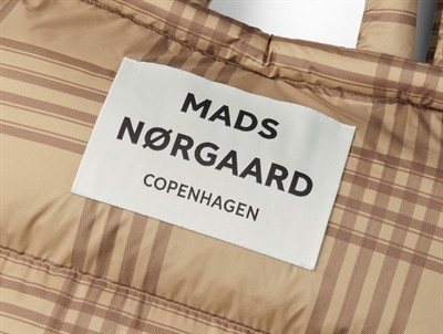 Nærbillede af logo på ternet puffertaske i beige og brun fra Mads Nørgaard
