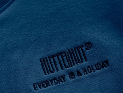 Detalje af blå Huttelihut sweatshirt med broderet logo foran